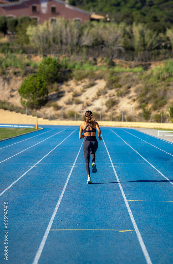 Beautiful young girl slim runner, dressed in tight sportswear, running towards the end of the curve of a blue running track. Beautiful young girl slim runner, dressed in tight sportswear, running towards the end of the curve of a blue running track.