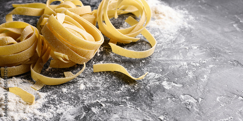 Homemade uncooked pasta fettuccine with flour over dark background