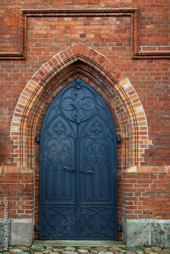 Metal door of an old church in a red brick masonry wall