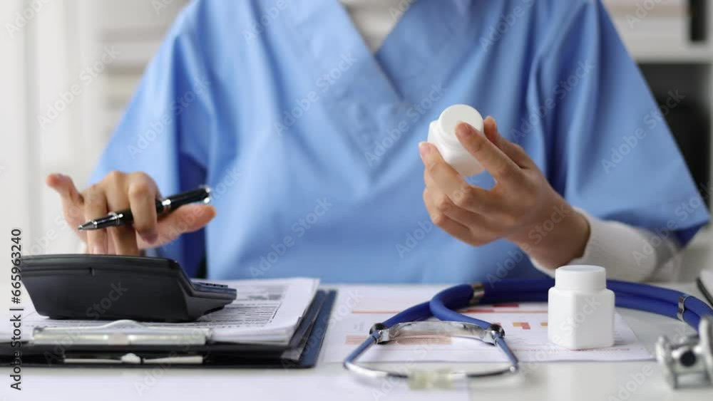Female doctor reading and writing prescriptions in hospital office. The doctor is calculating the dosage of medicine.