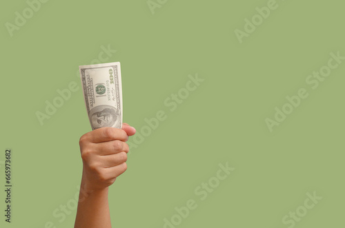 Close-up of hand holding US dollar bills against a green background.