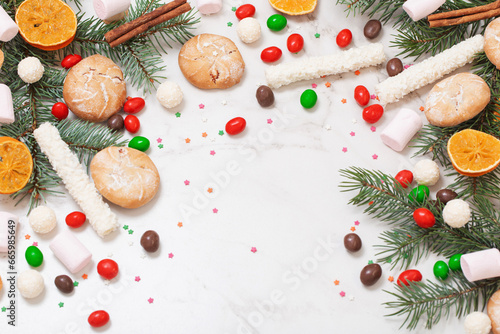 candies and cookies with christmas tree branches on white marble background
