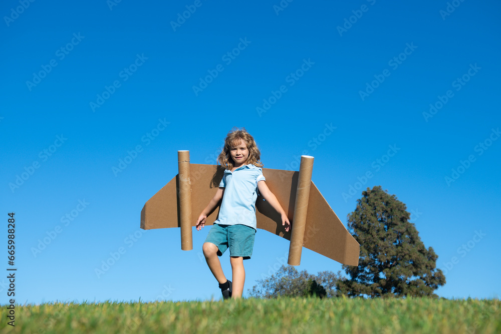 Little child plays astronaut or pilot. Child on the background of blue sky. Kids with paper wings jetpack dreams. Children imagines dreams of flying. Funny kid with toy jet pack. Success, imagination.