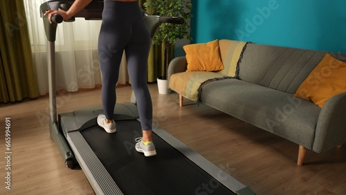Shot capturing young woman's legs. She is doing her morning cardio exercise, running on a threadmill. Home, room, indoor activities.