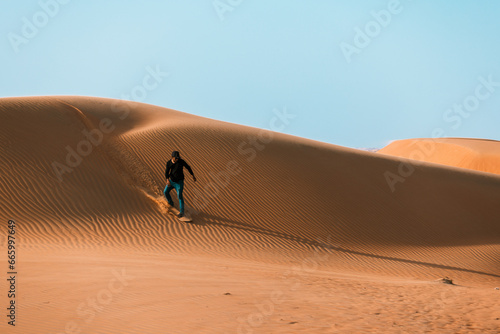 High quality stock photo of a man sliding down with a sand board in a dune in the Sultanate of Oman.