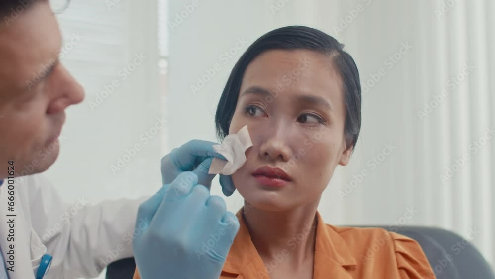 Medium close up of male doctor in white coat looking at nose of female patient after plastic surgery in clinic Medium close up of male doctor in white coat looking at nose of female patient after plastic surgery in clinic