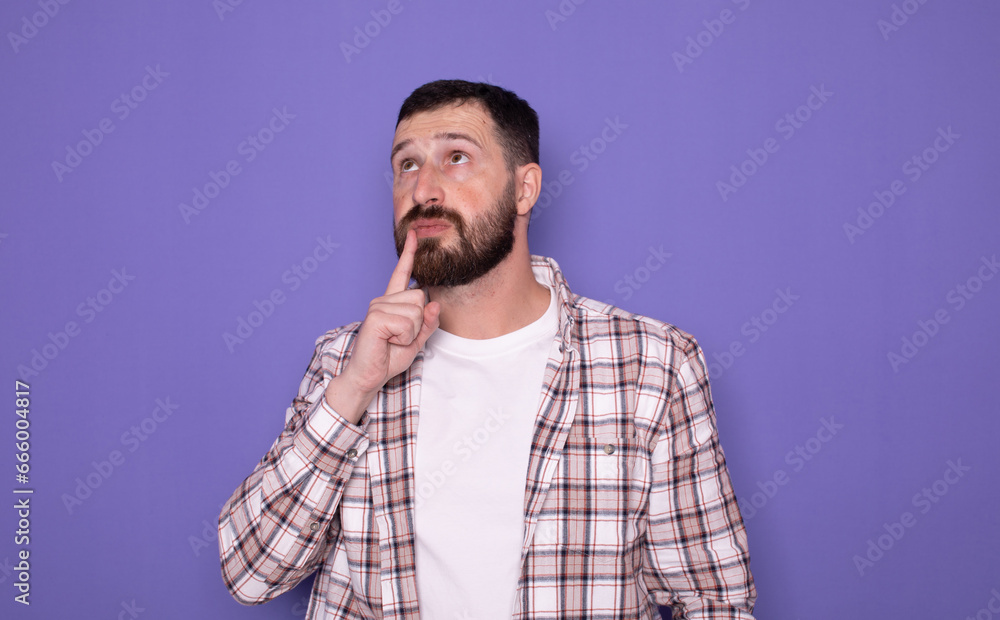 Caucasian handsome bearded man having doubts while looking up over isolated purple background. 