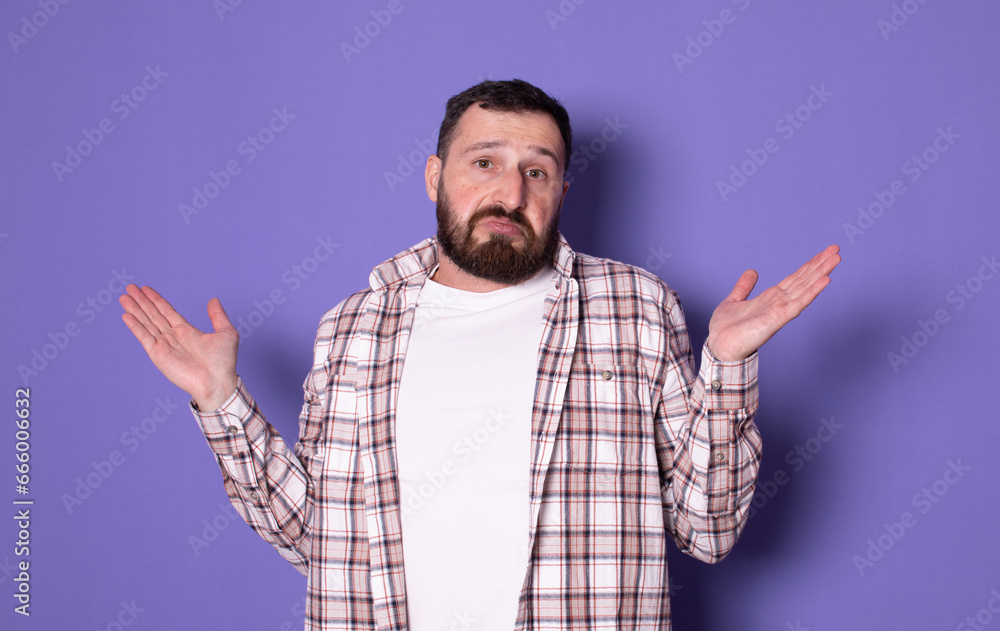 Portrait of confused bearded handsome bearded young man standing with raised arms, don't know what to do, isolated over purple background. I don't know. Portrait of confused bearded handsome bearded young man standing with raised arms, don't know what to do, isolated over purple background. I don't know.