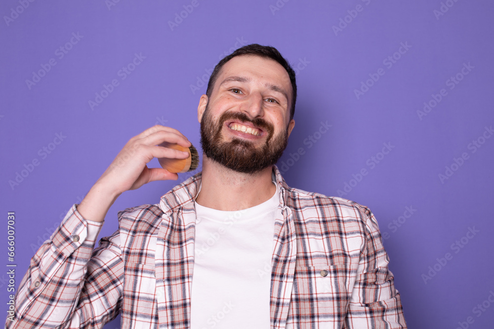 Handsome bearded man combing his beard with a brush on purple background. Handsome bearded man combing his beard with a brush on purple background.