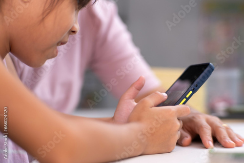 Happy Asian family mother and cute daughter using phone together at home. Mother and little girl laughing happily using smartphone watching funny social media video app sitting at table together.