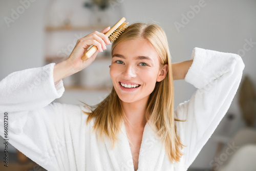 Portrait of happy blonde lady brushing her long hair indoor