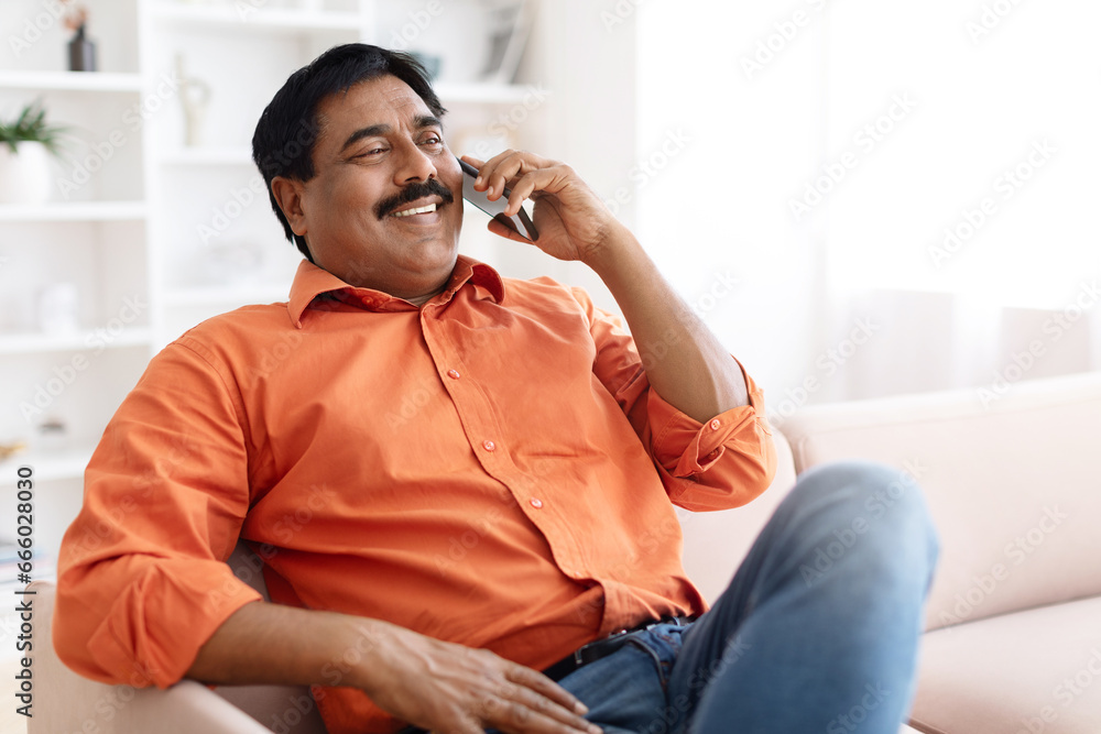 Happy middle aged indian man talking on phone at home Happy middle aged indian man talking on phone at home