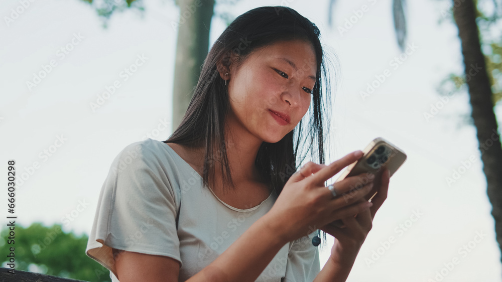 Close up, beautiful brunette girl sitting on bench in city park, using phone with mobile app, surfing social media, checking news