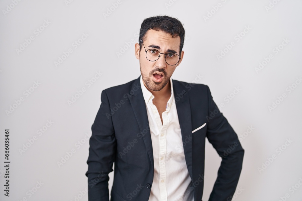 Handsome business hispanic man standing over white background in shock face, looking skeptical and sarcastic, surprised with open mouth Handsome business hispanic man standing over white background in shock face, looking skeptical and sarcastic, surprised with open mouth
