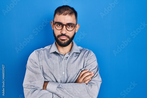 Middle east man with beard standing over blue background skeptic and nervous, disapproving expression on face with crossed arms. negative person.