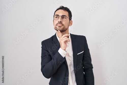 Handsome business hispanic man standing over white background thinking concentrated about doubt with finger on chin and looking up wondering