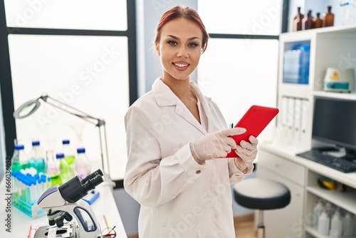 Young caucasian woman scientist smiling confident using touchpad at laboratory