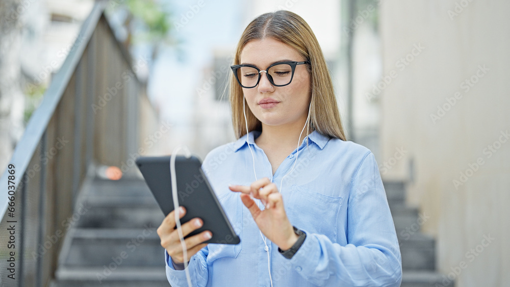 Young blonde woman business worker using touchpad and earphones at street