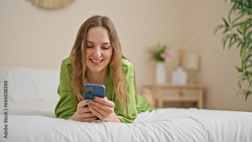 Young blonde woman using smartphone lying on bed at bedroom Young blonde woman using smartphone lying on bed at bedroom