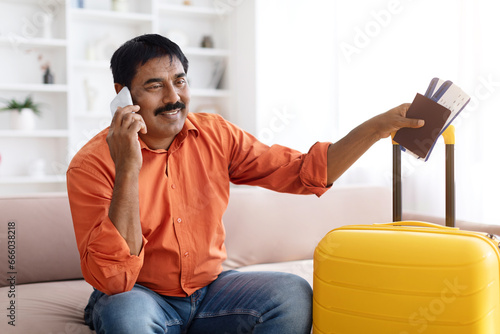 Happy mature indian man preparing for traveling, talking on phone photo