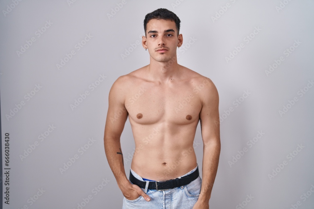 Handsome hispanic man standing shirtless relaxed with serious expression on face. simple and natural looking at the camera.