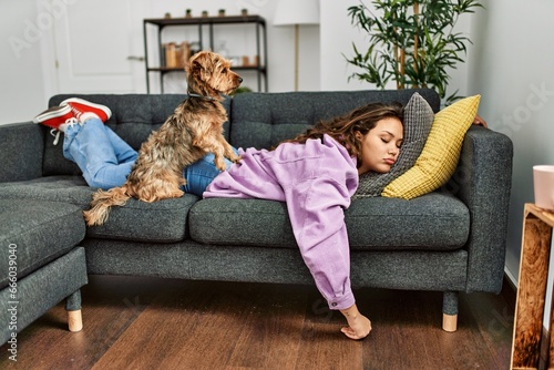 Young beautiful hispanic woman lying on sofa sleeping with dog at home