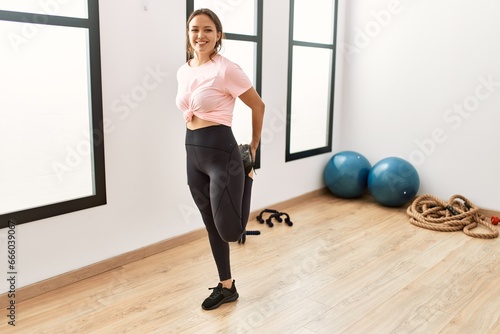 Young beautiful hispanic woman smiling confident stretching legs at sport center