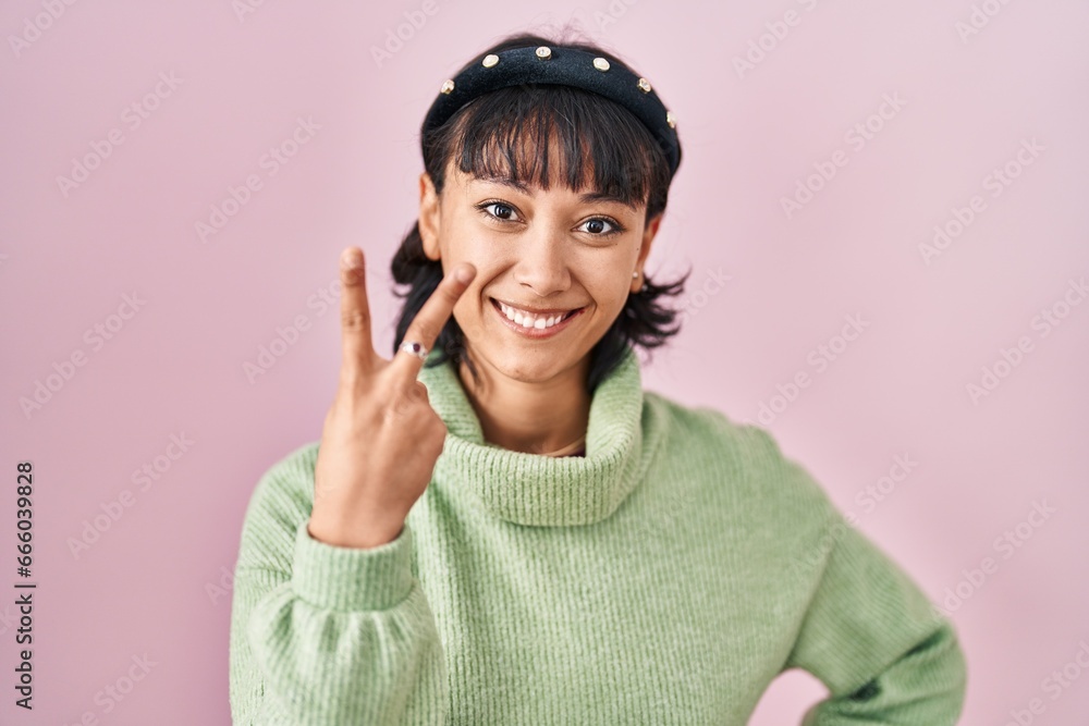 Young beautiful woman standing over pink background showing and pointing up with fingers number two while smiling confident and happy. Young beautiful woman standing over pink background showing and pointing up with fingers number two while smiling confident and happy.