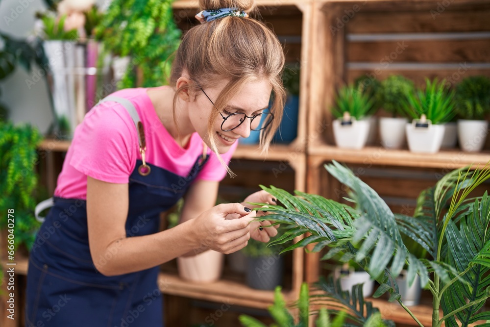 Obraz premium Young blonde woman florist smiling confident touching plant at flower shop