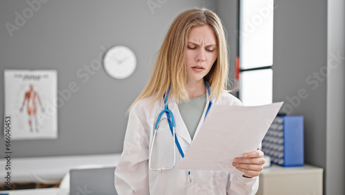 Young blonde woman doctor reading document at clinic