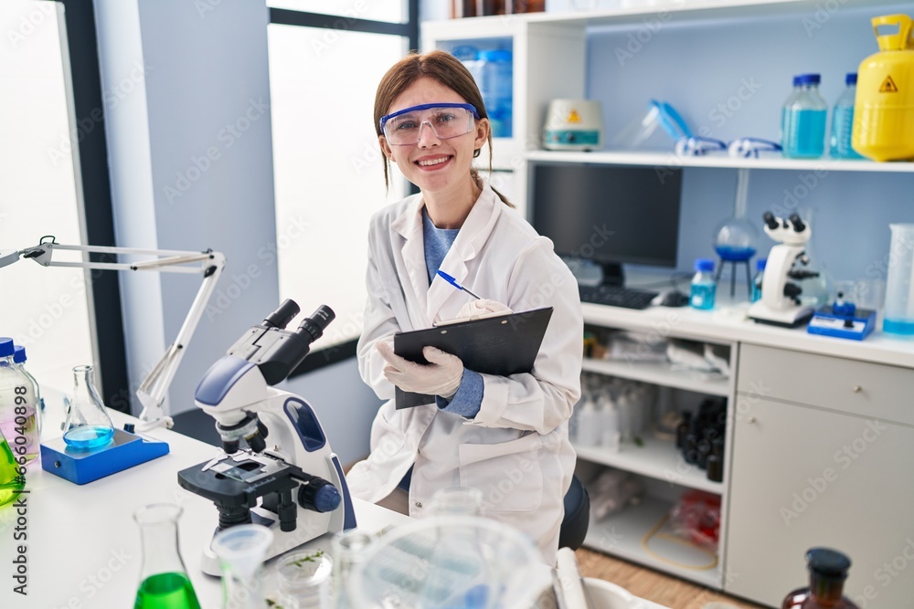 Young blonde woman scientist using microscope writing on document at laboratory Young blonde woman scientist using microscope writing on document at laboratory