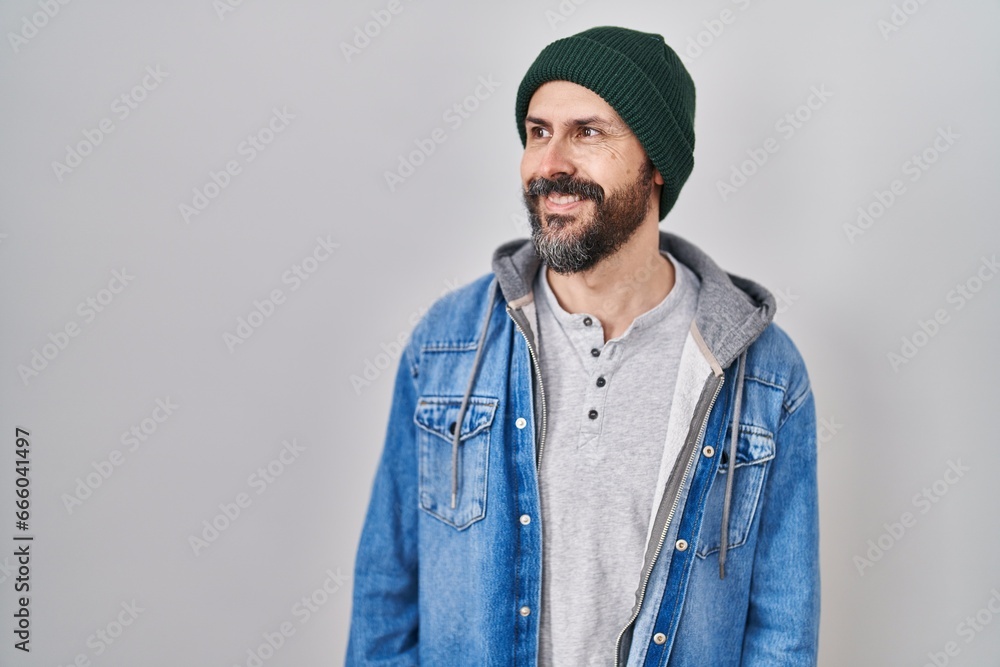 Fototapeta premium Young hispanic man with tattoos wearing wool cap looking away to side with smile on face, natural expression. laughing confident.