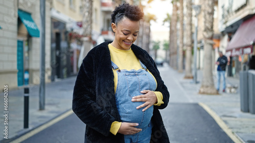 Young pregnant woman smiling confident touching belly at street © Krakenimages.com