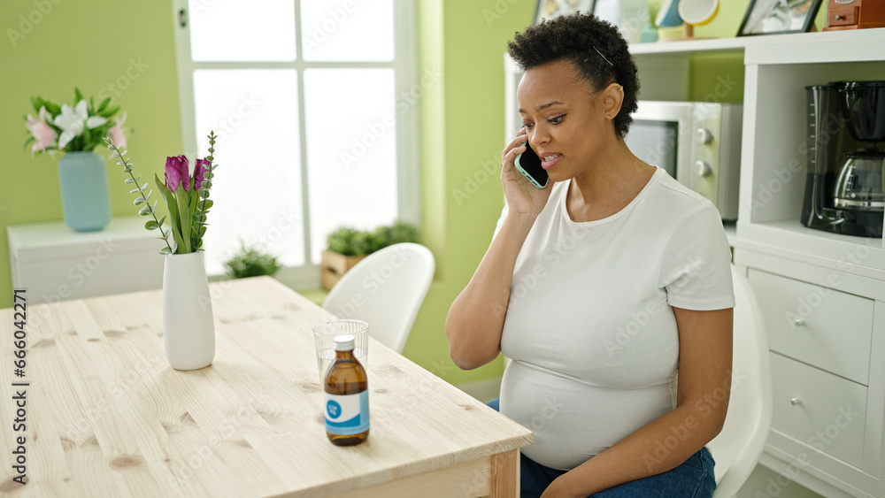 Young pregnant woman having medical phone consultation sitting on table at dinning room Young pregnant woman having medical phone consultation sitting on table at dinning room