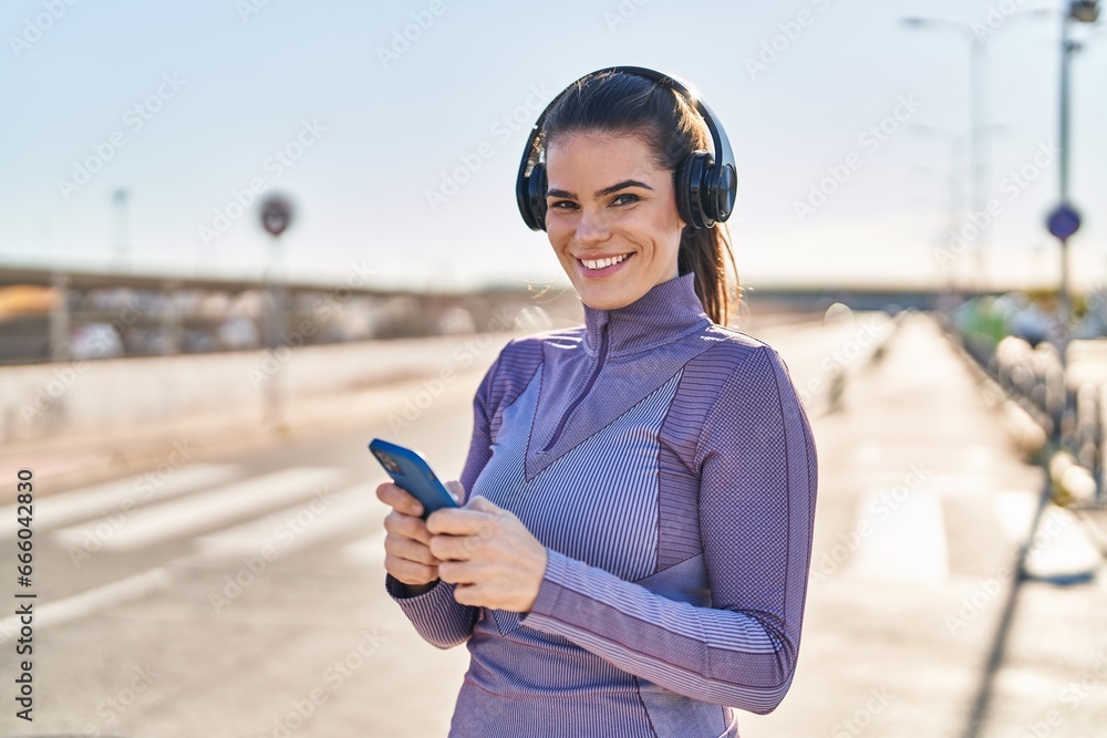 Young beautiful hispanic woman wearing sportswear listening to music at street