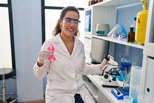 Young hispanic woman working at scientist laboratory looking for breast cancer cure winking looking at the camera with sexy expression  cheerful and happy face.