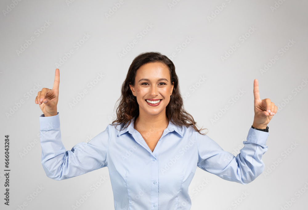 Happy adult european woman in formal wear pointing fingers up at empty space Happy adult european woman in formal wear pointing fingers up at empty space