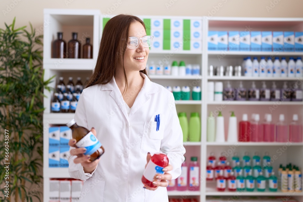 Young beautiful woman pharmacist smiling confident holding medication bottles at pharmacy