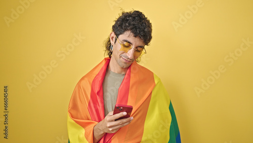 Young hispanic man wearing rainbow flag using smartphone over isolated yellow background © Krakenimages.com