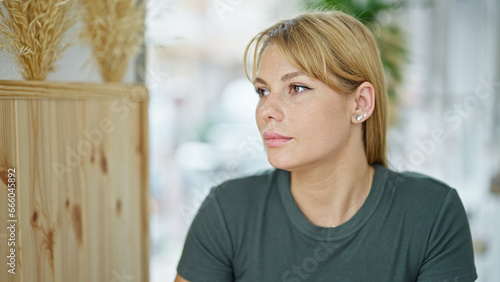 Schilderij op canvas Young blonde woman sitting on table looking to the side at coffee shop