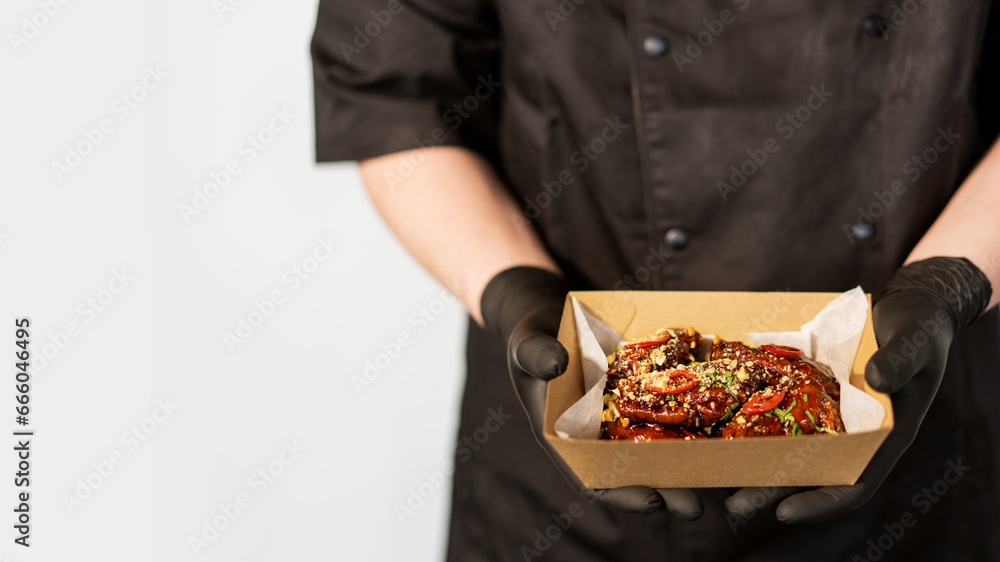 The cook holds in his hands a box with grilled spicy chicken