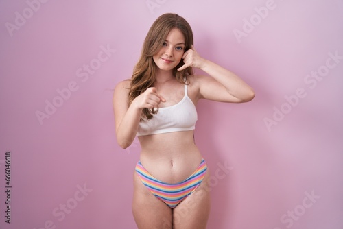 Caucasian woman wearing lingerie over pink background smiling doing talking on the telephone gesture and pointing to you. call me. © Krakenimages.com