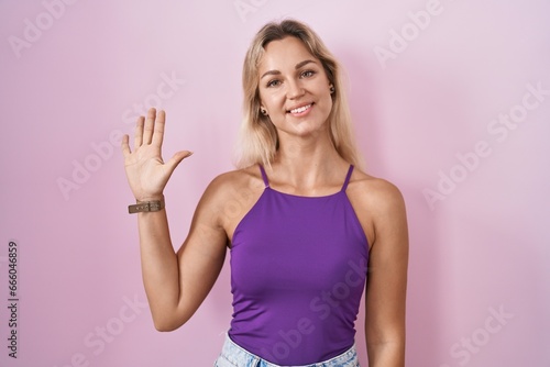 Young blonde woman standing over pink background showing and pointing up with fingers number five while smiling confident and happy. © Krakenimages.com