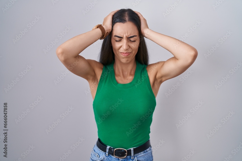 Young woman standing over isolated background suffering from headache desperate and stressed because pain and migraine. hands on head. Young woman standing over isolated background suffering from headache desperate and stressed because pain and migraine. hands on head.