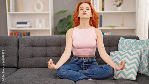 Young redhead woman doing yoga exercise sitting on sofa at home