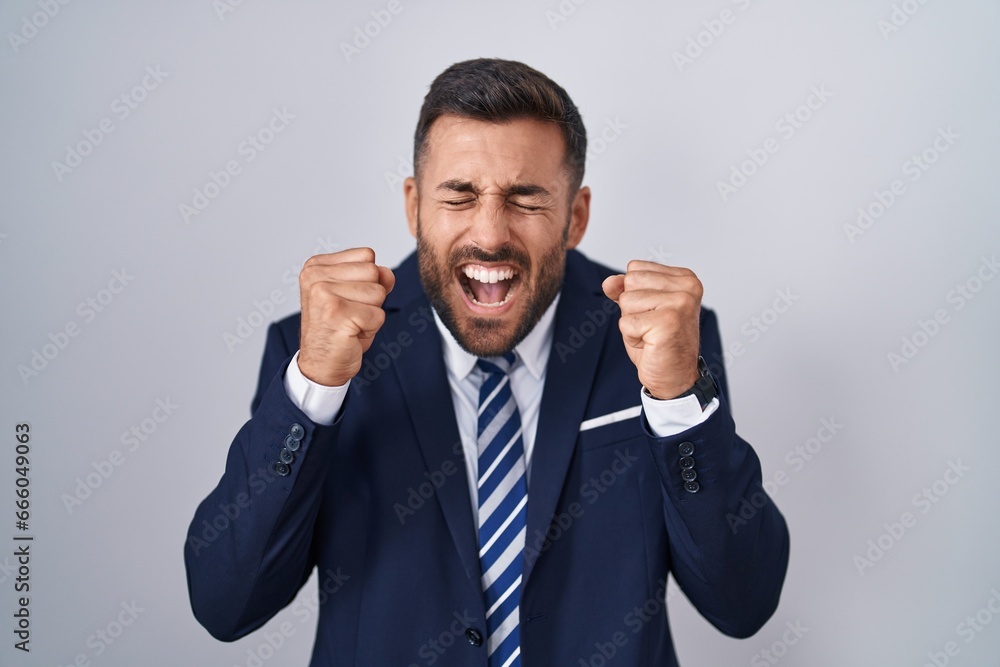Handsome hispanic man wearing suit and tie excited for success with arms raised and eyes closed celebrating victory smiling. winner concept. Handsome hispanic man wearing suit and tie excited for success with arms raised and eyes closed celebrating victory smiling. winner concept.