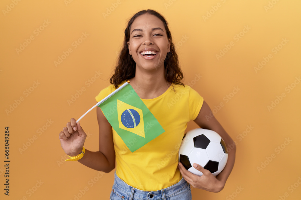 Young hispanic woman holding brazil flag and football ball smiling and laughing hard out loud because funny crazy joke. Young hispanic woman holding brazil flag and football ball smiling and laughing hard out loud because funny crazy joke.