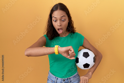 Young hispanic woman holding ball looking at the watch time worried  afraid of getting late
