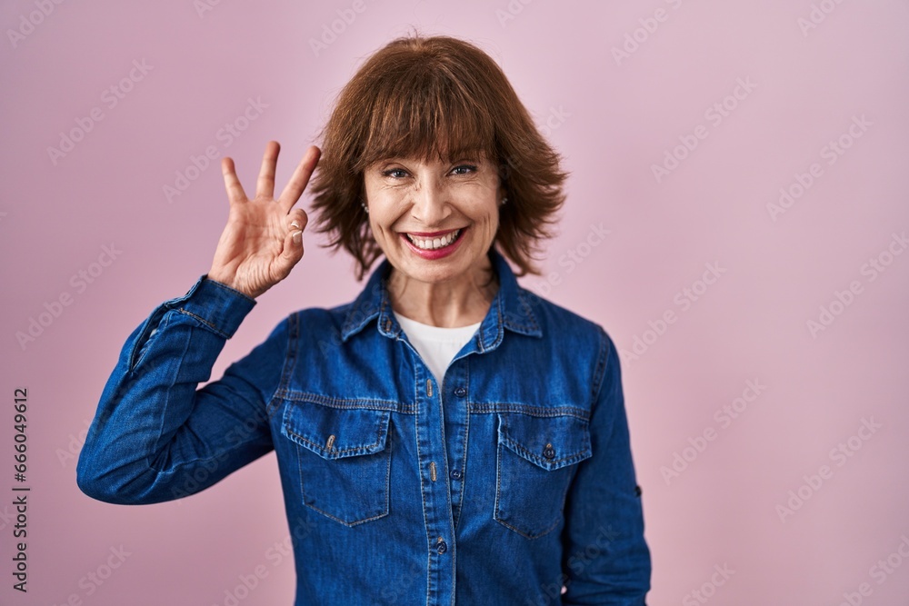 Middle age woman standing over pink background smiling positive doing ok sign with hand and fingers. successful expression. Middle age woman standing over pink background smiling positive doing ok sign with hand and fingers. successful expression.