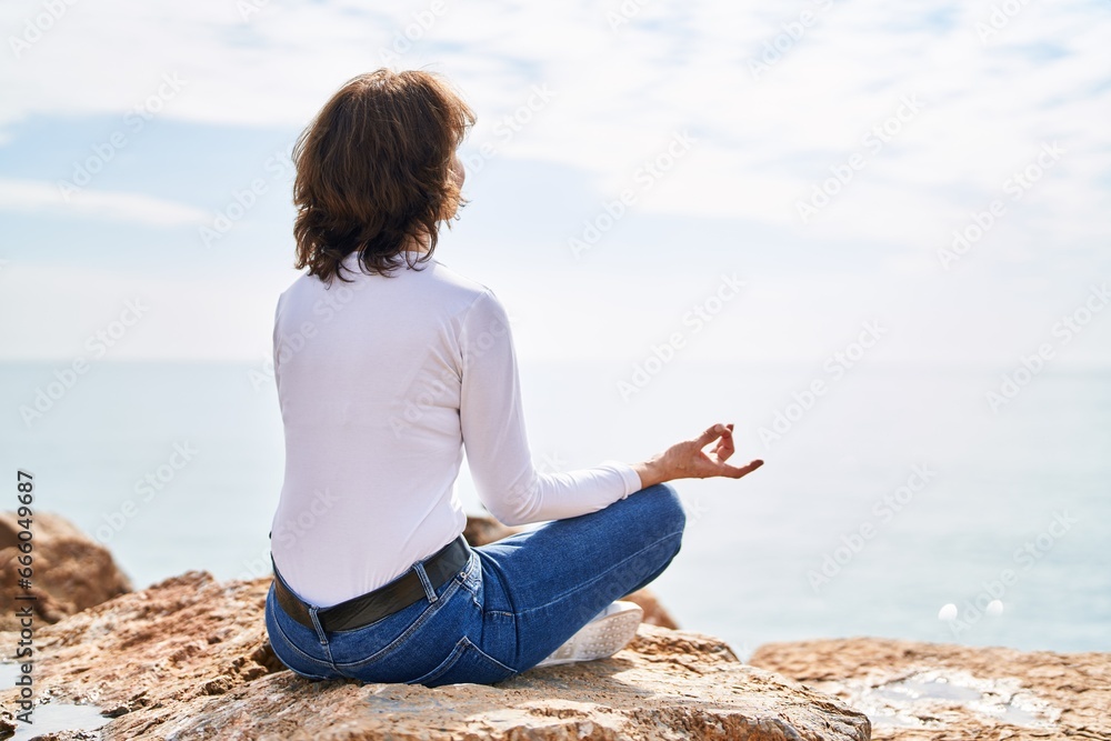 Middle age woman doing yoga exercise sitting on the rock at seaside